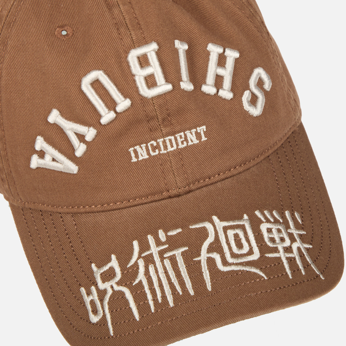 Close-up of the Brown Shibuya Incident Hat inspired by Jujutsu Kaisen, featuring white embroidered text and Japanese characters on the front and brim.