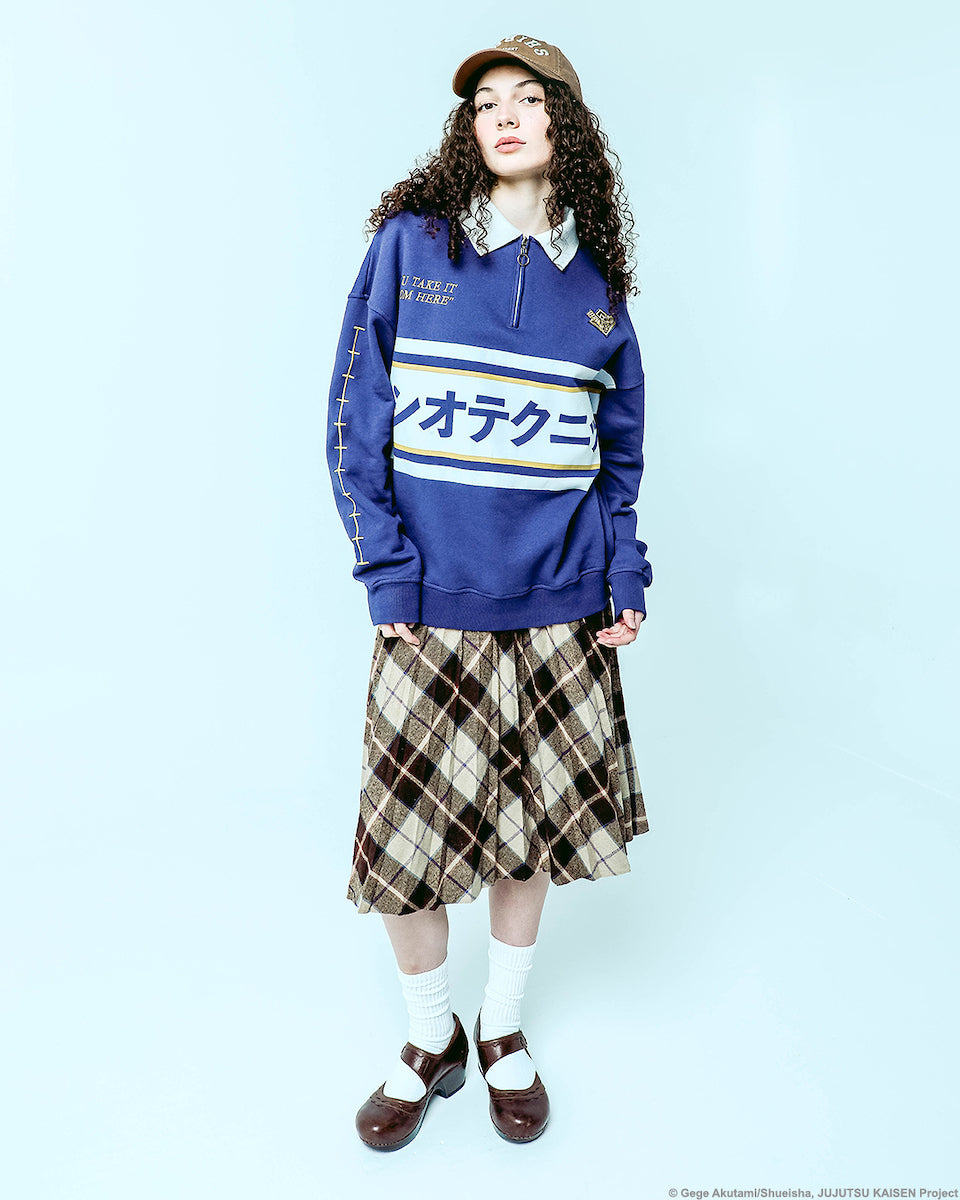 Female modeling Atsuko Kento Nanami Blue & Yellow Quarter-Zip Pullover with a navy blue base, white and yellow stripes, Japanese text across the chest, and a white collar with a ring zipper on a pale blue background.