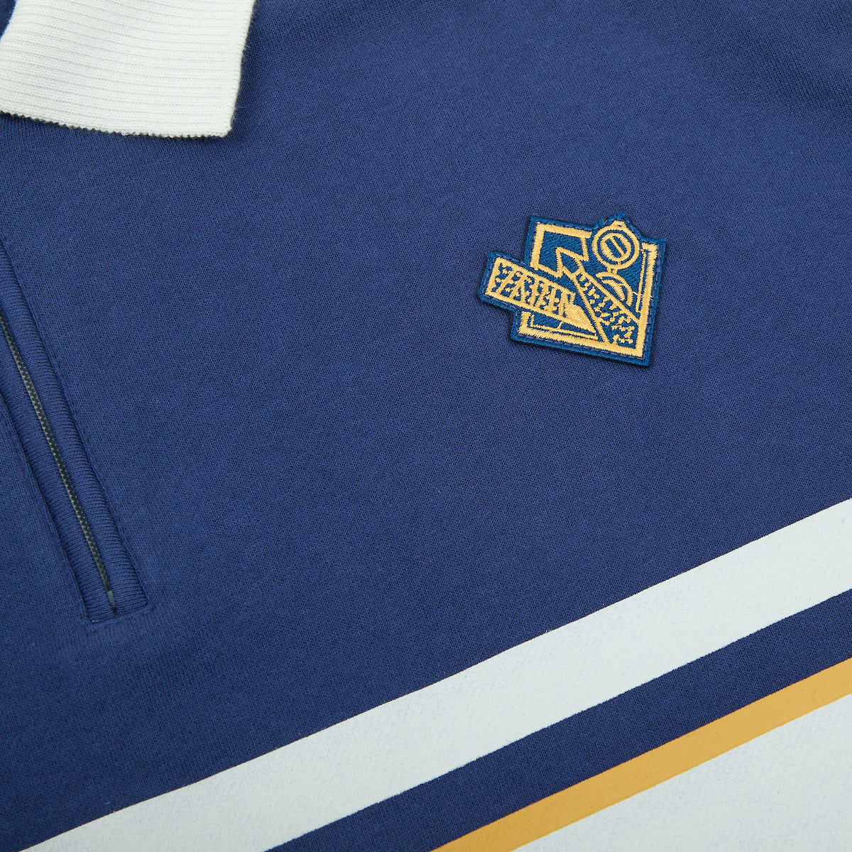 Close up of the patch on the Atsuko Kento Nanami Blue & Yellow Quarter-Zip Pullover with a navy blue base, white and yellow stripes, Japanese text across the chest, and a white collar with a ring zipper.